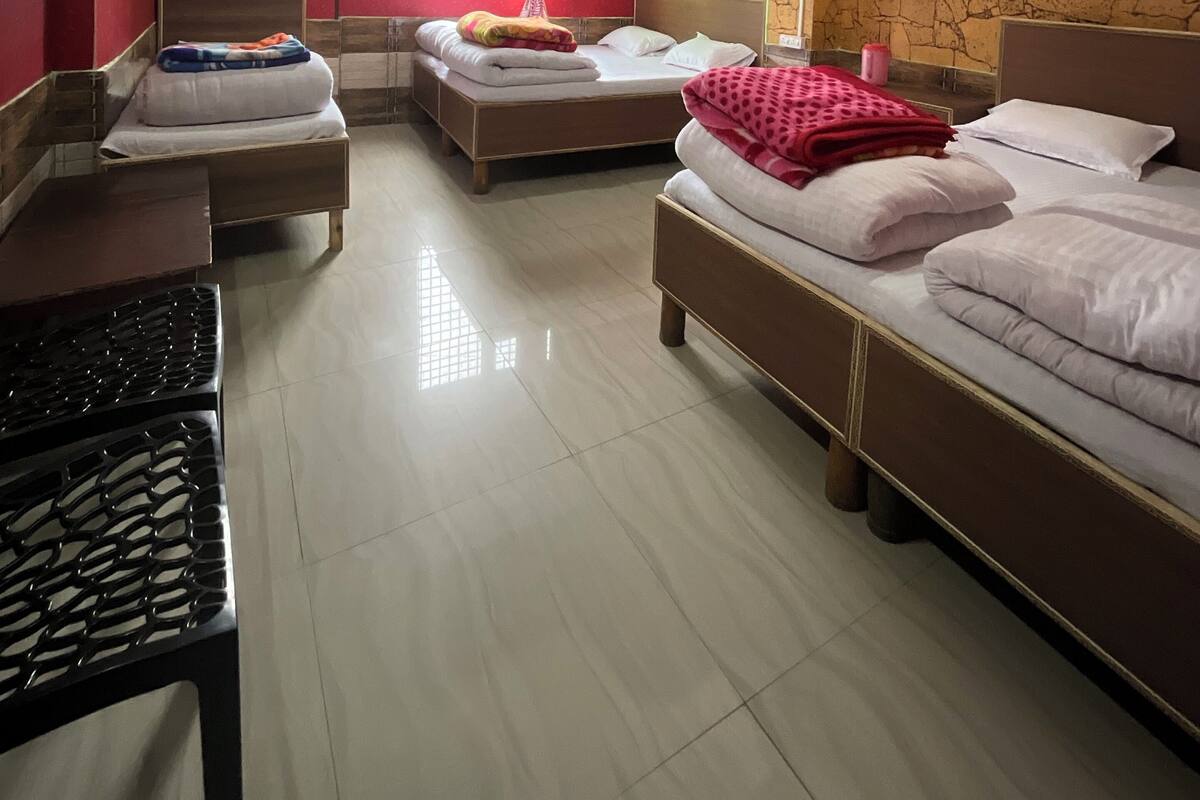 A hotel room with three beds, a ceiling fan, a window with curtains, and a tiled floor.