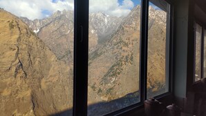 A room with a large window offering a view of rugged mountains and a valley. - J M S Guest House (Joshimath)