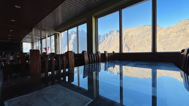 A conference room with a glass table and chairs, large windows with a mountain view, and a menu on the table. - J M S Guest House (Joshimath)
