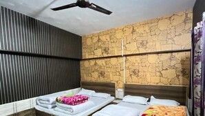 A room with two beds, a ceiling fan, a stone wall, and a window with curtains. - J M S Guest House (Joshimath)