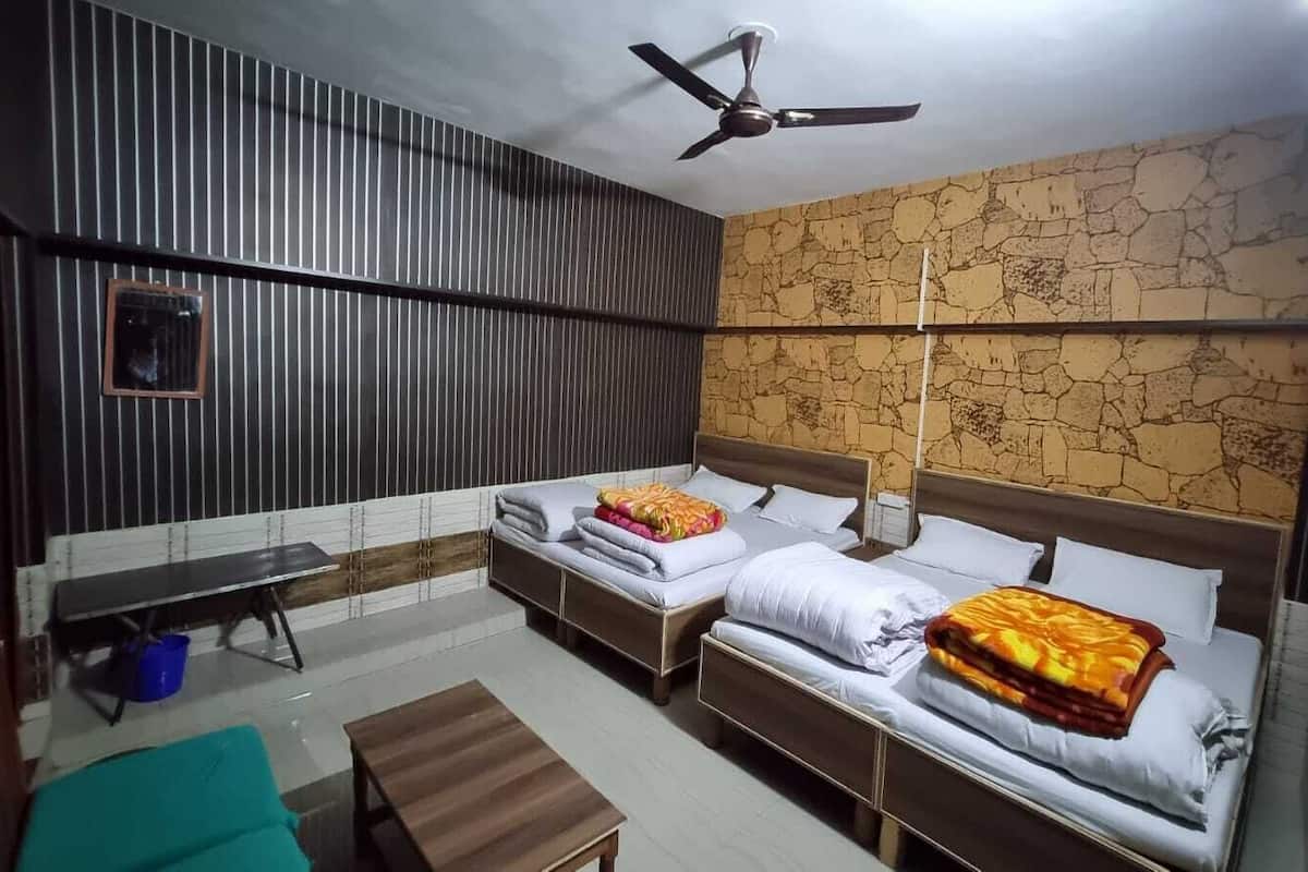 A hotel room with two single beds, a bench, a ceiling fan, and a stone-patterned wall.