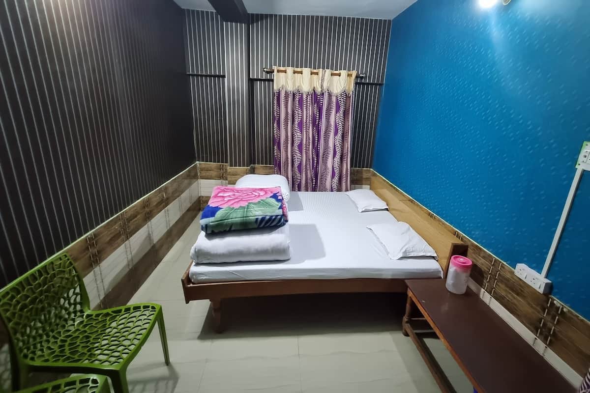 A room with a bed, a green chair, a bedside table, and a wall socket.