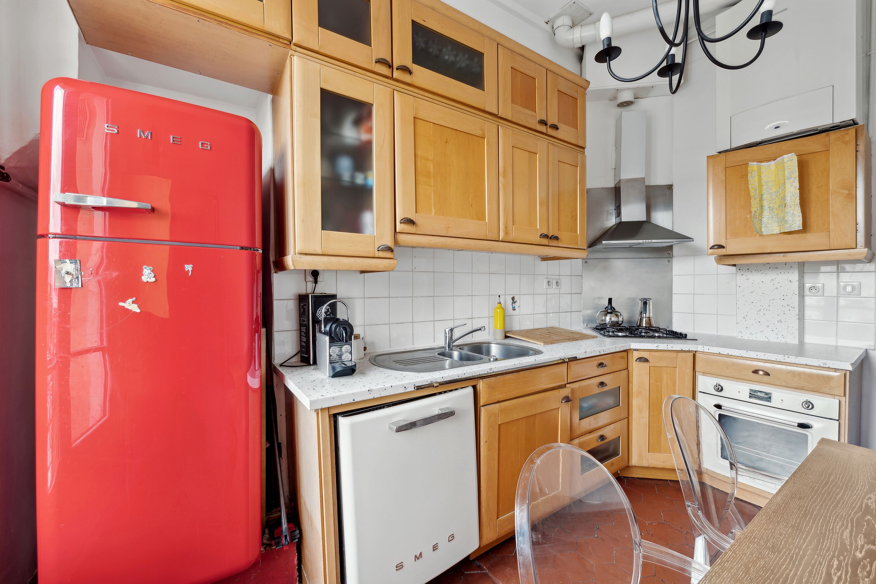 Eine Küche mit Holzausstattung, einem roten Kühlschrank, einem weißen Geschirrspüler und einem transparenten Stuhl.