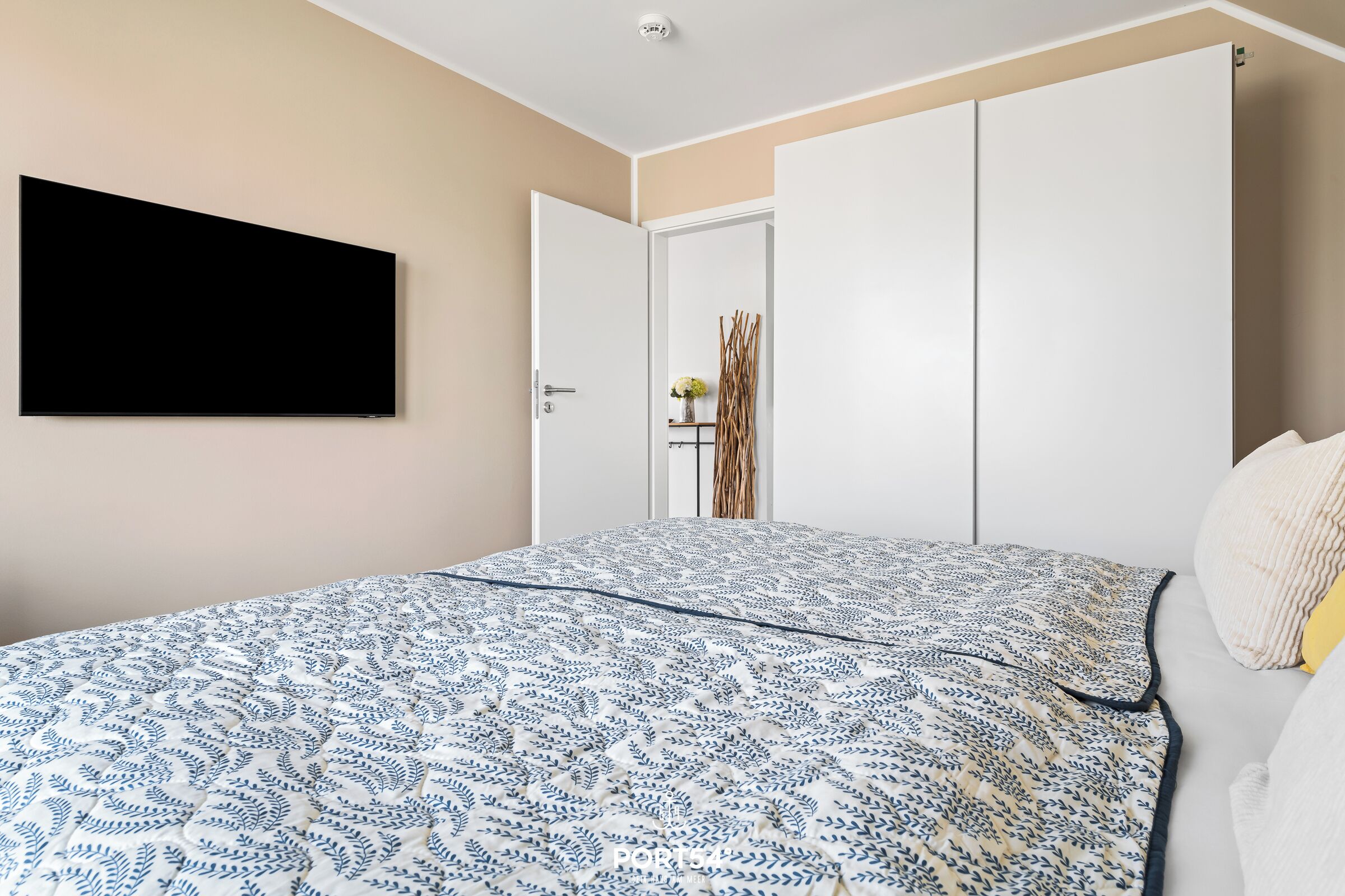 A bedroom with a bed, a TV mounted on the wall, and a wardrobe.