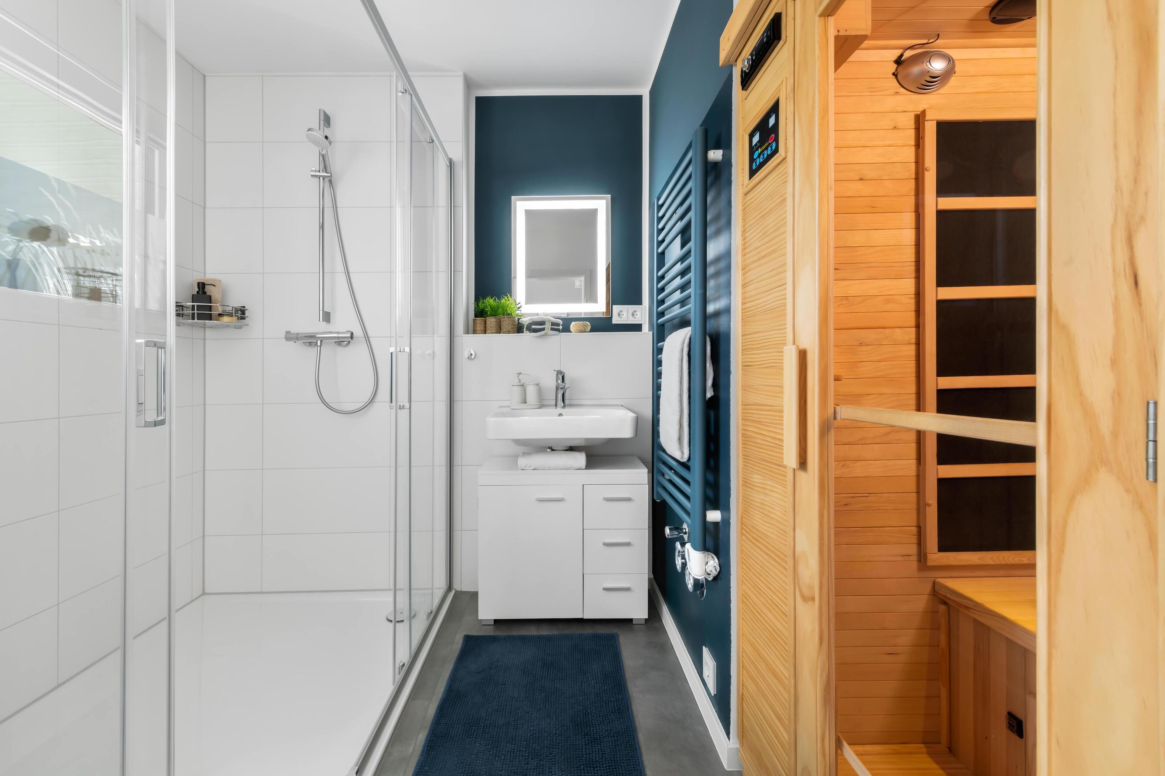 A modern bathroom with a walk-in shower, a sink, and a wooden sauna.