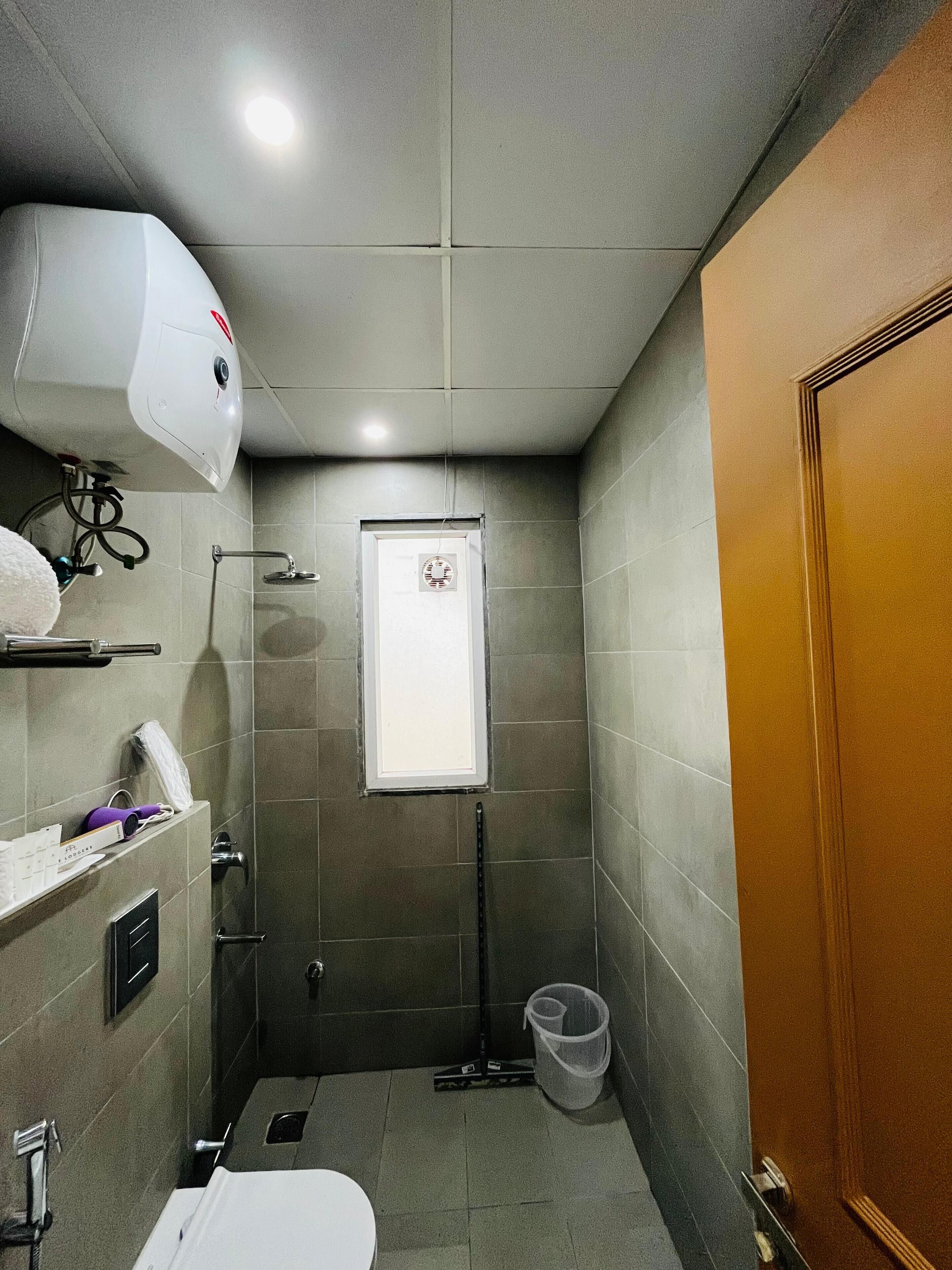 A small, tiled bathroom with a toilet, a hand dryer, a showerhead, and a door.