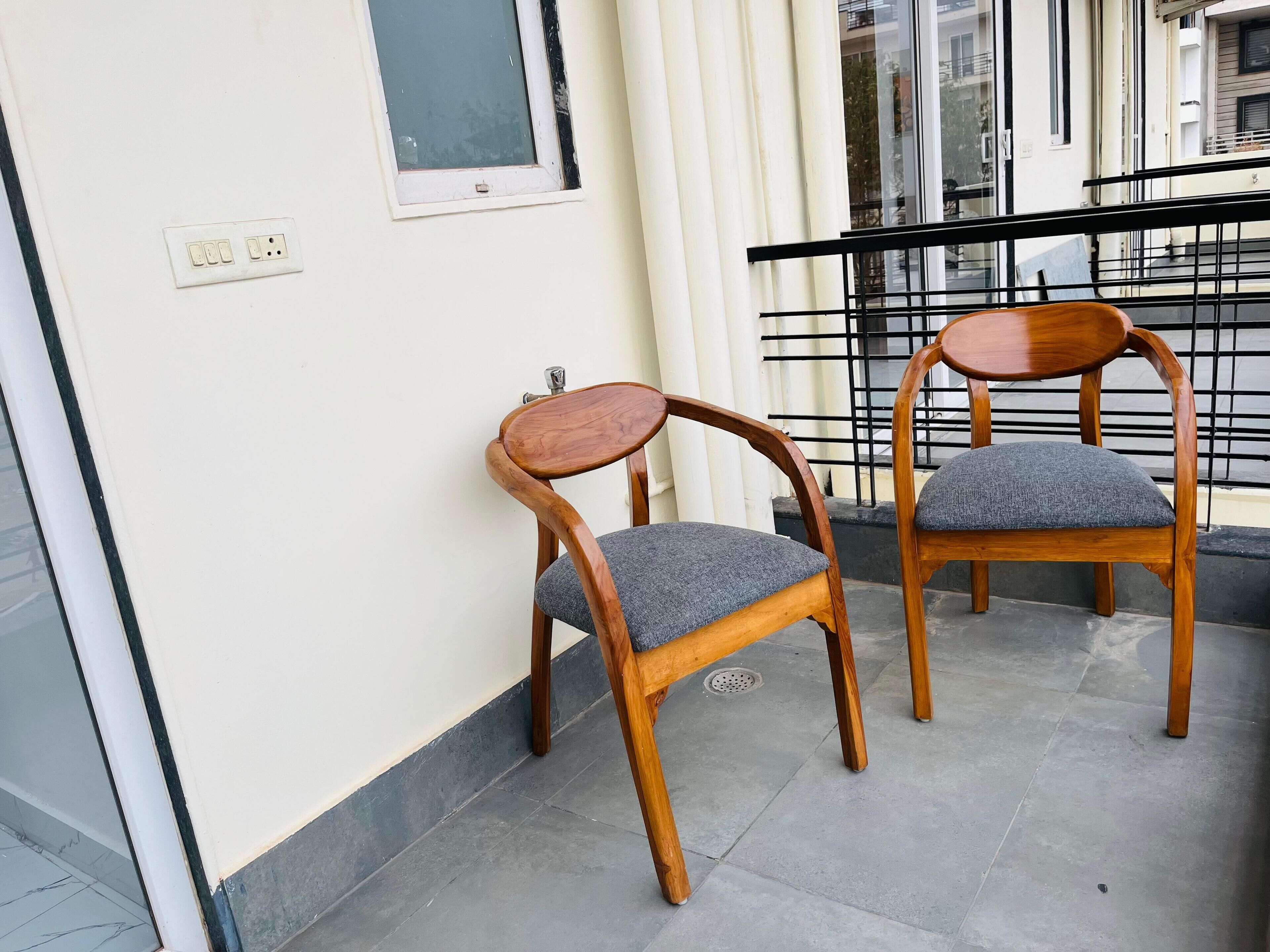 Two wooden chairs with grey cushions on a balcony.