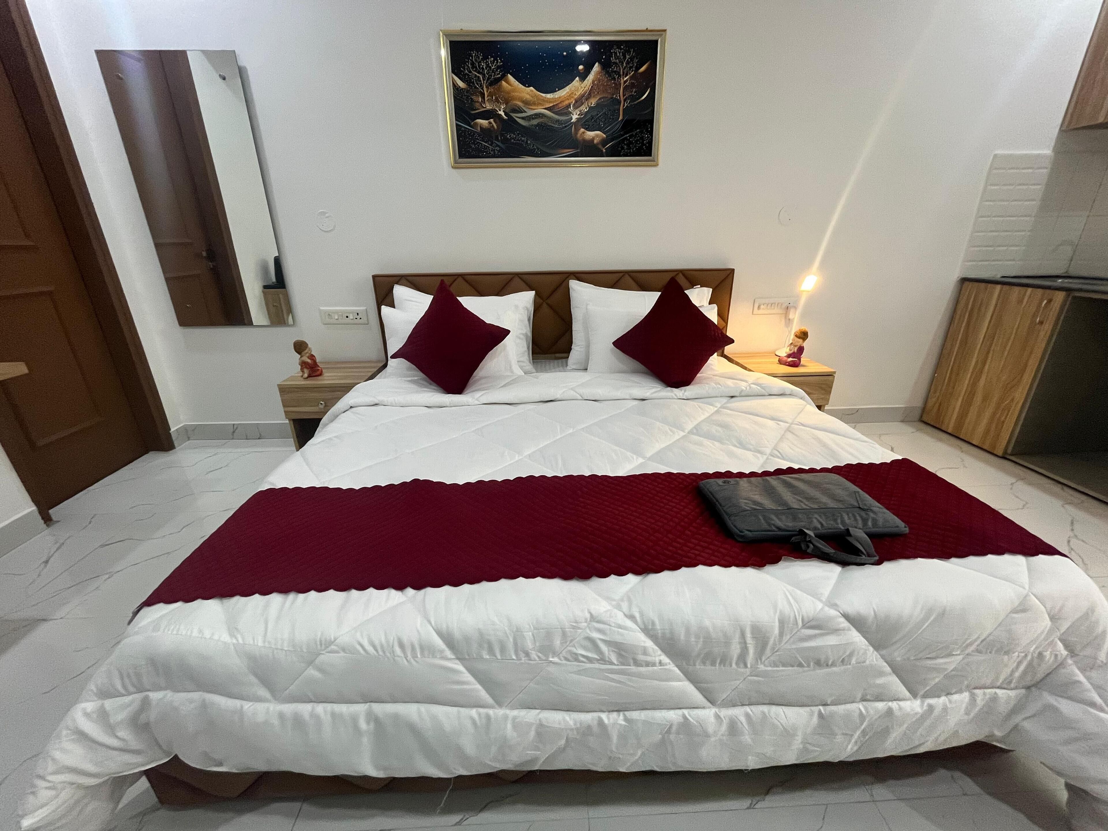 A neatly made bed with white and red bedding, a nightstand with a lamp, and a painting on the wall.