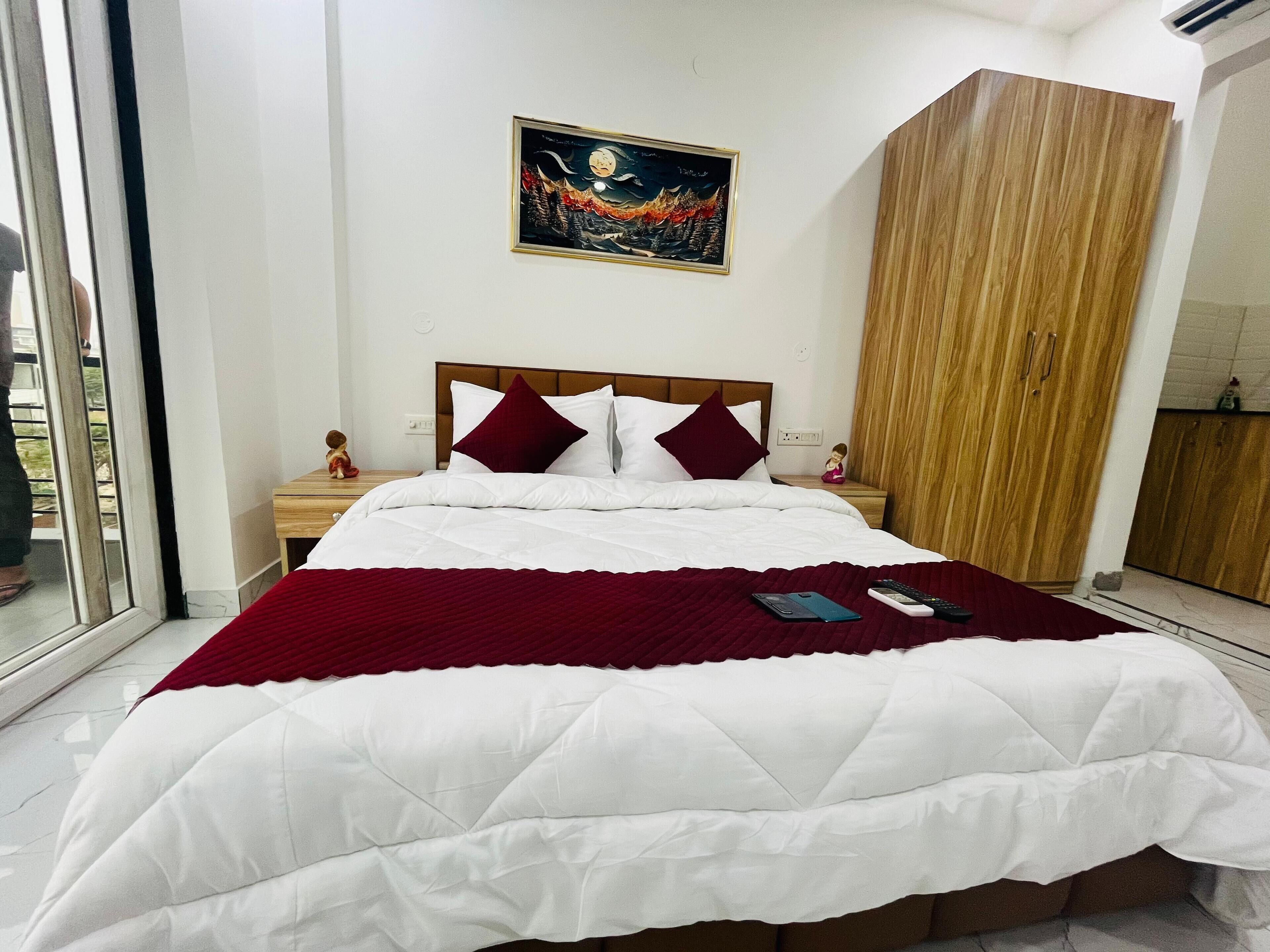 A neatly made bed with white and red bedding, a wooden headboard, a nightstand with a figurine, and a painting on the wall.