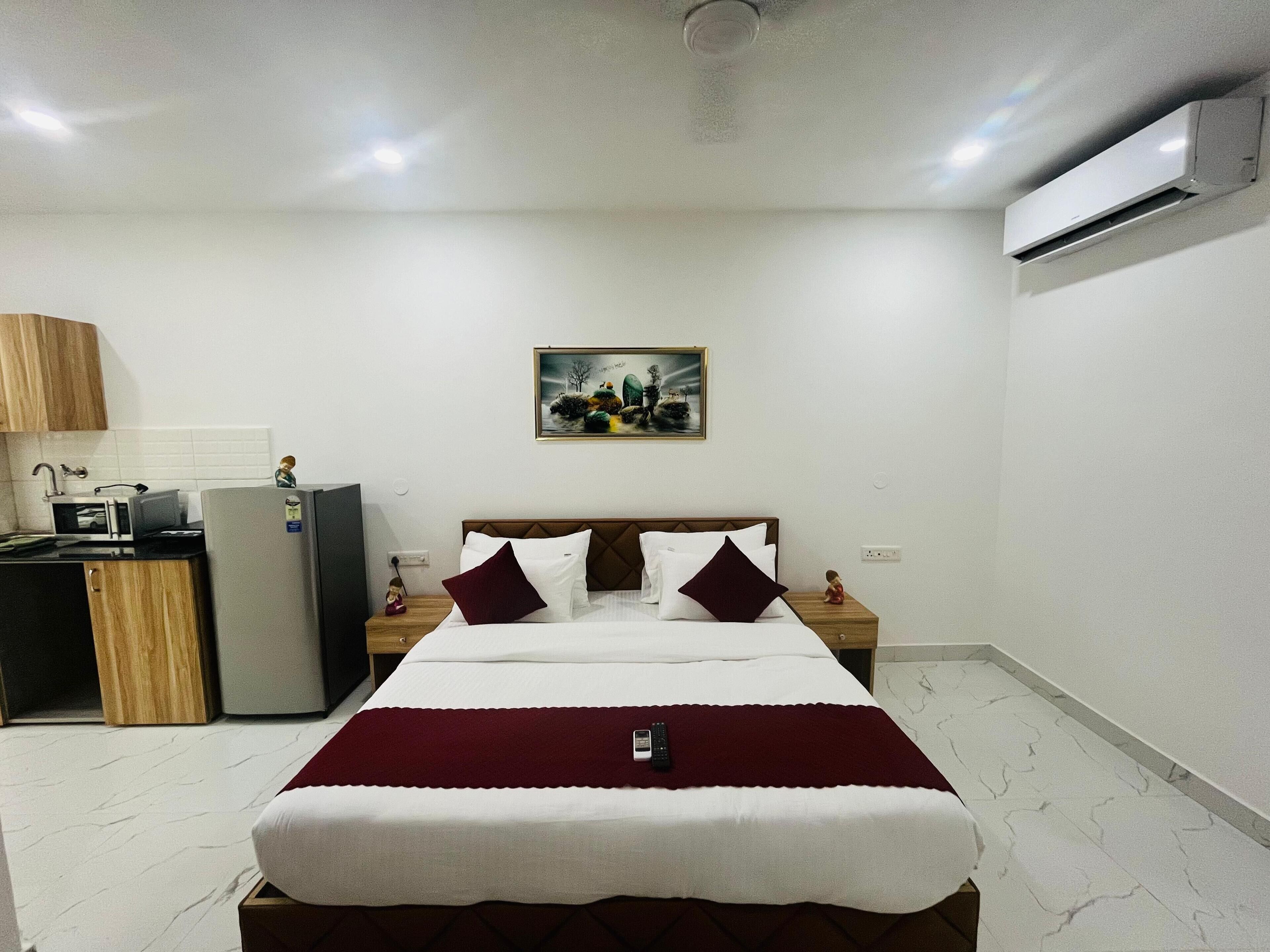 A hotel room with a bed, a desk with a computer, a microwave, and an air conditioner.