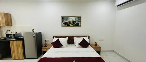 A hotel room with a bed, a desk with a computer, a microwave, and an air conditioner.