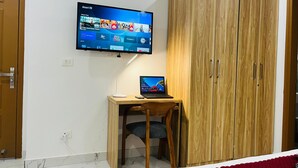 Una habitación con un armario de madera, un escritorio con una computadora portátil y un televisor montado que muestra la interfaz de un servicio de streaming.