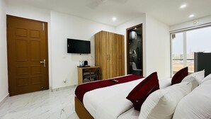 Habitación de hotel con cama, televisor, armario de madera, escritorio con silla y baño visible a través de una puerta abierta.