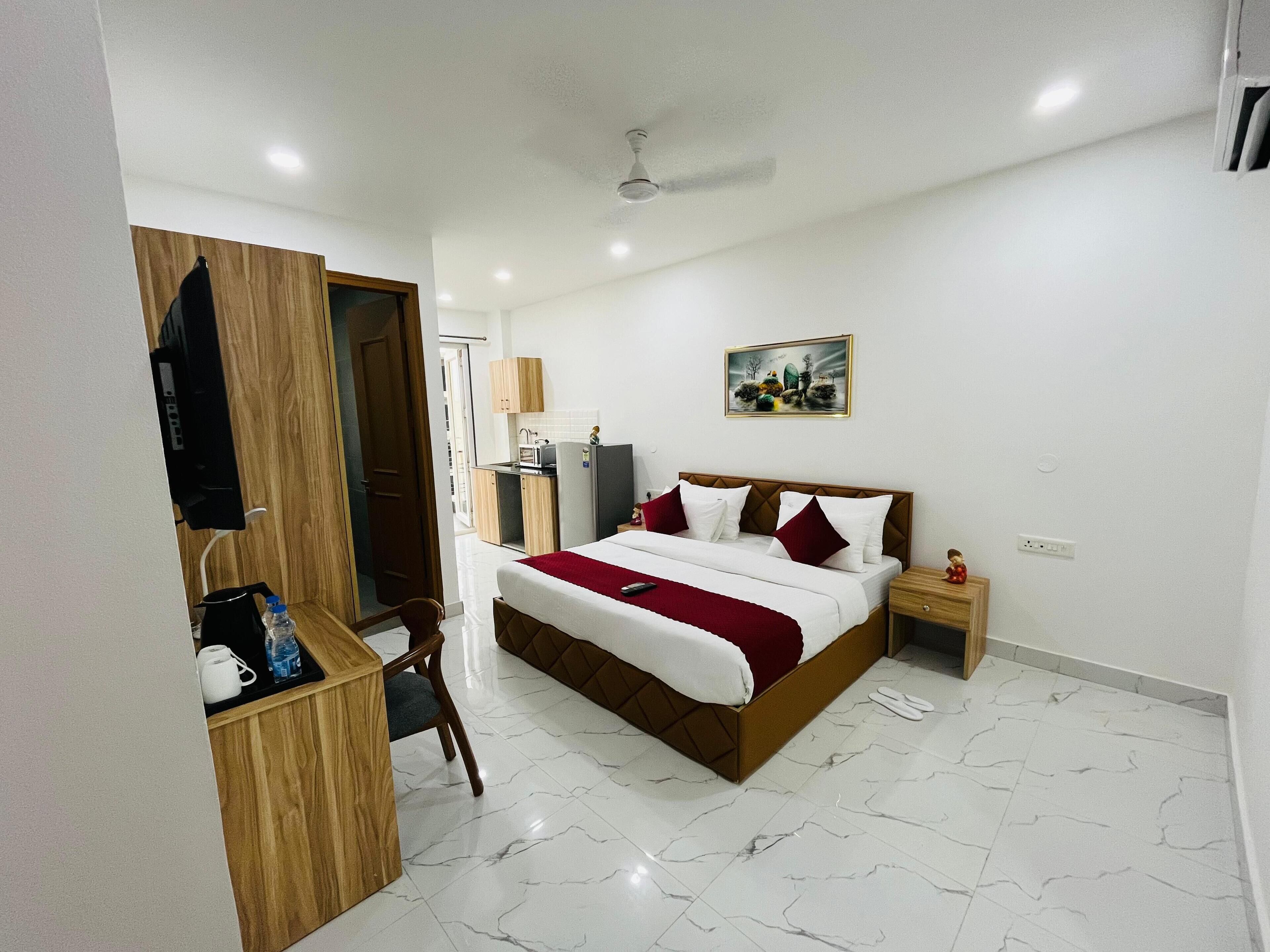 Habitación de hotel con cama, escritorio con silla, kitchenette pequeño y ventilador de techo.