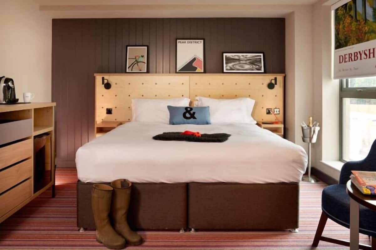 A hotel room with a large bed, a wooden nightstand, a desk, and a chair. There are framed pictures on the wall and a poster on the wall.