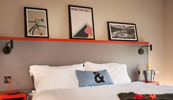 Una habitación de hotel con una cama, un estante rojo con marcos de fotos, una mesita de noche y una lámpara.