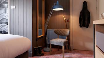 Habitación de hotel con cama, escritorio, silla, lámpara de pie y perchero.