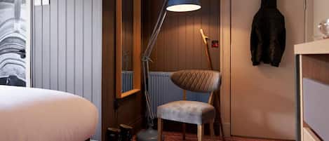 Une chambre d’hôtel comprenant un lit, un bureau, une chaise, une lampe sur pied et un porte-manteau.