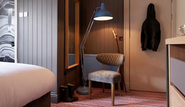 Habitación de hotel con cama, escritorio, silla, lámpara de pie y perchero.