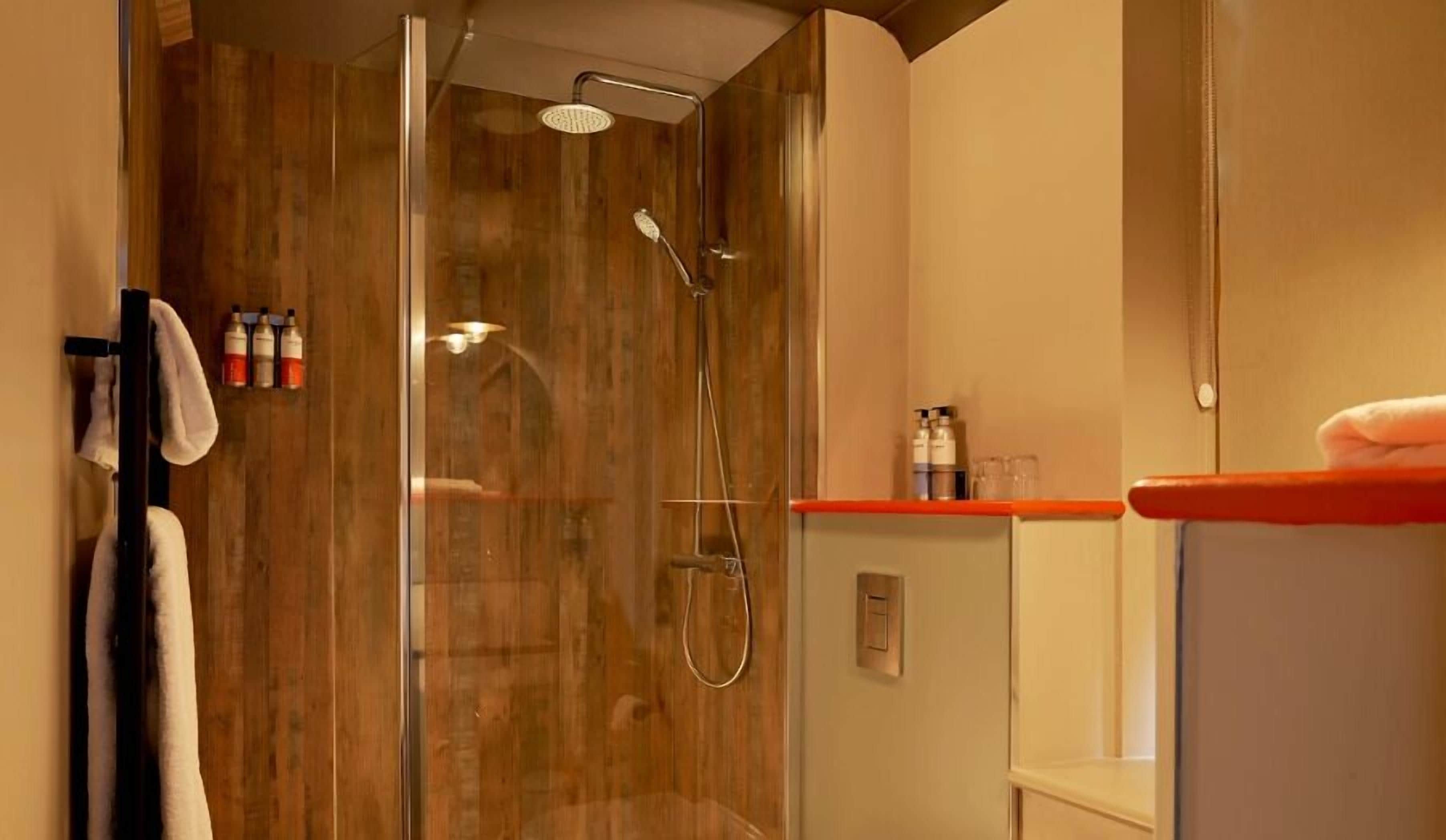 Un baño moderno con ducha de vidrio, lavamanos blanco sobre encimera roja y artículos de aseo en la pared.