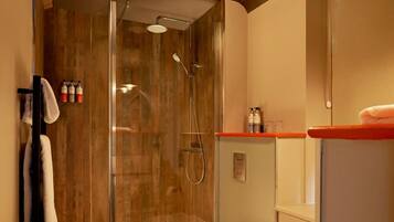 Un baño moderno con ducha de vidrio, lavamanos blanco sobre encimera roja y artículos de aseo en la pared.