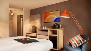 Une chambre d’hôtel avec un lit, un bureau et une chaise, une machine à café et un téléviseur fixé au mur.