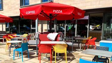 Outdoor seating with red umbrellas labeled "COFFEE," "PIZZA," and "GRILLS."