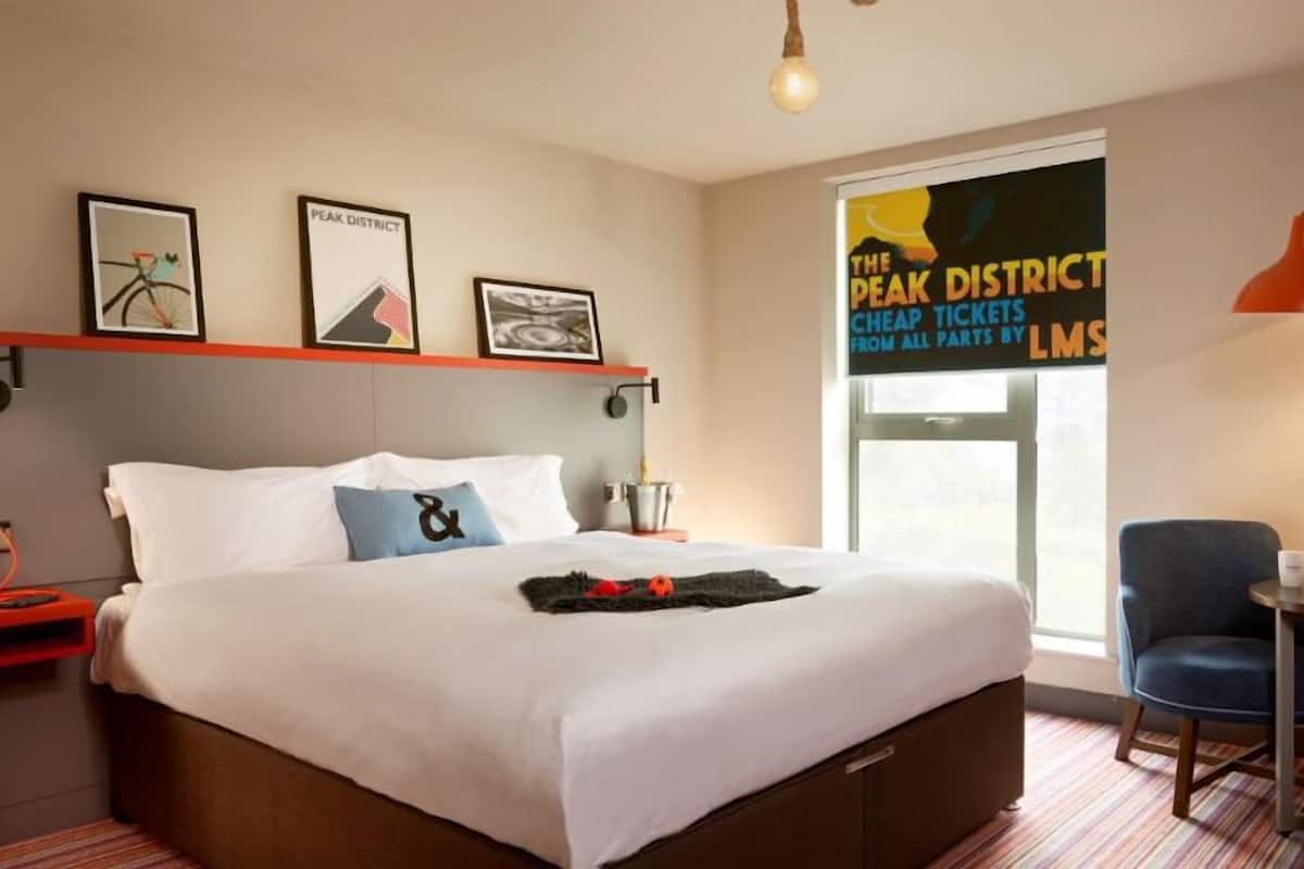 A hotel room with a large bed, a desk with a chair, a window with a view, and a wall with framed pictures.