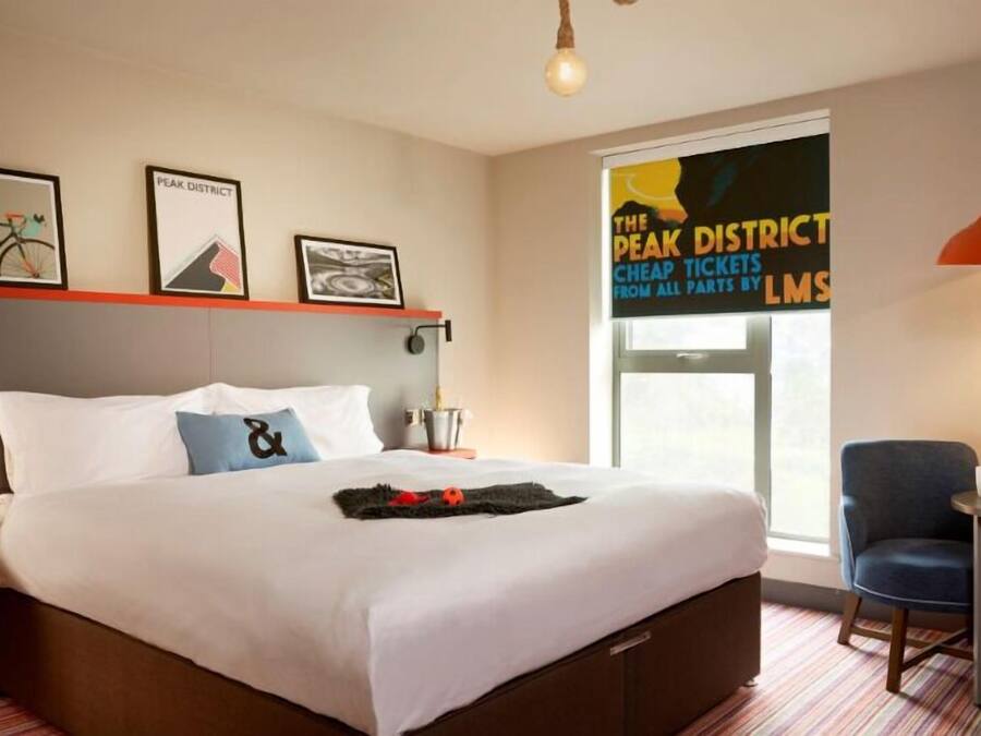A hotel room with a large bed, a desk with a chair, a window with a view, and a wall with framed pictures.