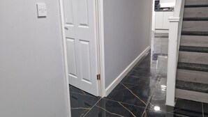 Un pasillo con una puerta blanca, una escalera de escalones grises y una zona de cocina al fondo.