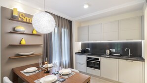 A modern kitchen with a dining area, featuring a wooden table set for dining, a built-in oven, and a large pendant light. - Suite Odyssée 2 - Five Star Holiday House (Saint-Jean-Cap-Ferrat)