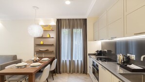 A modern kitchen with a dining area, featuring a wooden table set for four, a hanging light fixture, and built-in cabinets. - Suite Odyssée 2 - Five Star Holiday House (Saint-Jean-Cap-Ferrat)