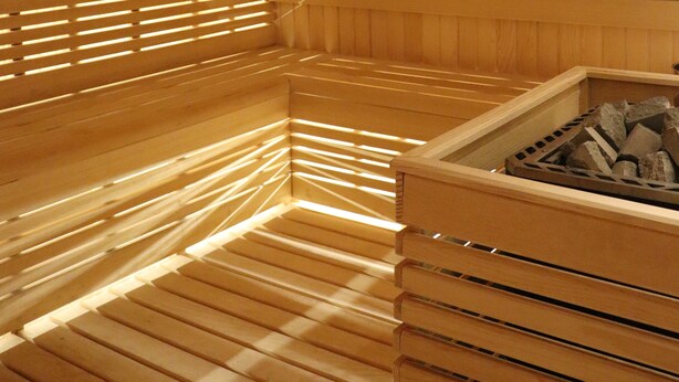 Una sauna de madera con bancos y un calentador central.