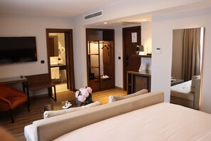 A hotel room with a bed, a desk, a chair, a TV, a mirror, and a bathroom visible through an open door. - Riva Hotel Nisantasi & Spa (Istanbul)