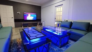 A modern living room with a flat-screen TV, a sofa, and illuminated coffee tables. - Seremban Grande Villa by uBook (Seremban)