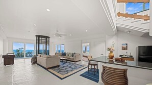 A spacious living area with a large sofa set, a dining table, and a kitchen area with a TV. - Waterfalling Estate is an oceanfront compound on the Big Island unlike any other (Ninole)