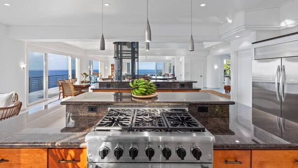 A spacious kitchen with a central island, a stainless steel refrigerator, and a view of the ocean. - Waterfalling Estate is an oceanfront compound on the Big Island unlike any other (Ninole)