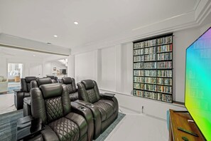 A modern living room with leather recliners, a large bookshelf, and a flat-screen TV. - Waterfalling Estate is an oceanfront compound on the Big Island unlike any other (Ninole)