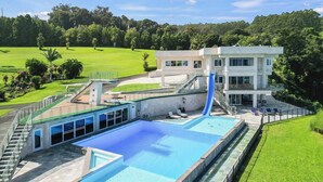 A modern hotel with a large swimming pool, a slide, and a well-maintained lawn. - Waterfalling Estate is an oceanfront compound on the Big Island unlike any other (Ninole)