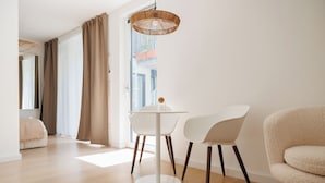 A modern living room with a round white table, two white chairs, a beige armchair, and a woven floor lamp. - BOHO City Suites Augarten (Vienna)