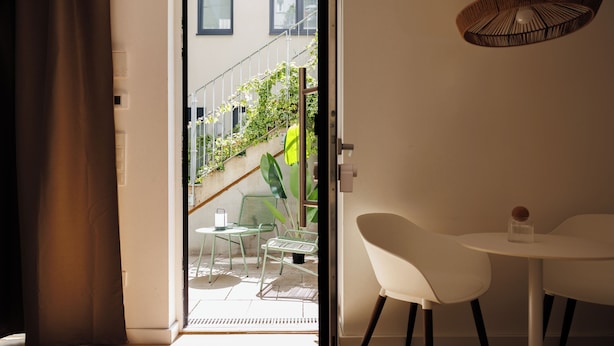 A modern room with a sliding glass door leading to a balcony with outdoor furniture and plants. - BOHO City Suites Augarten (Vienna)