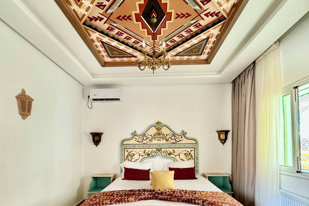 A bedroom with a patterned ceiling, a bed with a green and white headboard, and a bench.