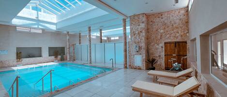 Una piscina interior con tragaluces, suelo de baldosas y sillas de descanso.
