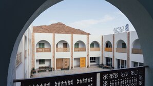 A courtyard with a building featuring multiple arches and a sandy hill in the background. - Capsa Thermal Oasis (Gafsa)