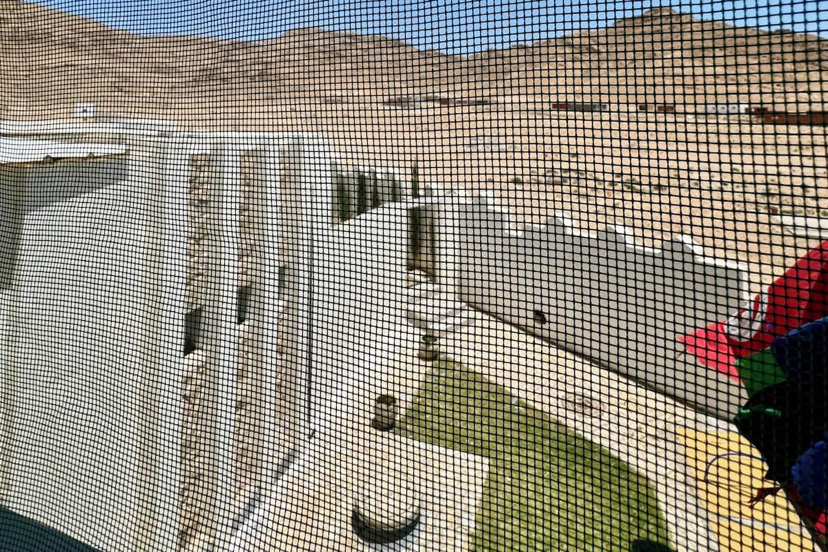 A close-up of a netted enclosure with a sandy ground and a blue sky visible through the gaps.