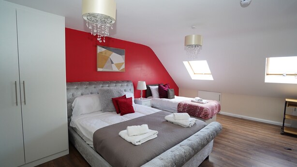 A bedroom with a large bed, a smaller bed, a wardrobe, a chandelier, a ceiling light, and a skylight. - 59B Comfortable Home Sleeps 8 (Hounslow)