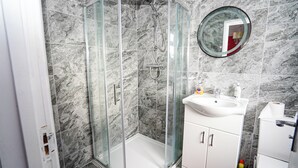 A bathroom with a glass-enclosed shower, a white sink with a mirror, and marble tiles. - 59B Comfortable Home Sleeps 8 (Hounslow)