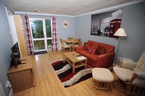 A living room with a red sofa, wooden coffee table, and a red and black striped rug. There is a dining table with chairs, a lamp, and a painting of a red telephone booth. - Tranquil Retreat in St Albans (St Albans)