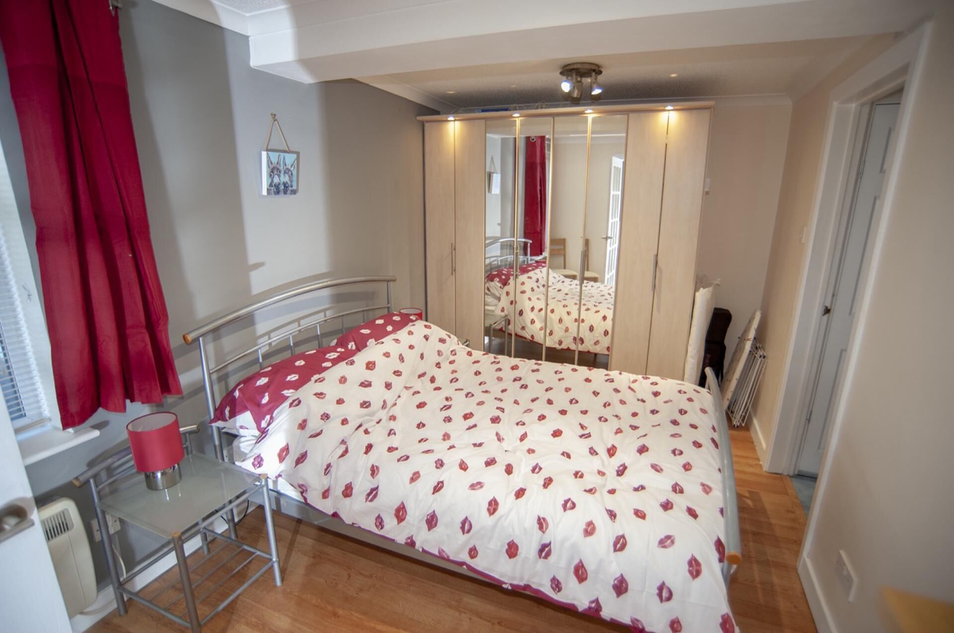 A bedroom with a bed, a mirror, a radiator, and a window with curtains.
