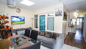 Un salón con un sofá gris, una mesa de centro de cristal y un televisor que muestra un paisaje.